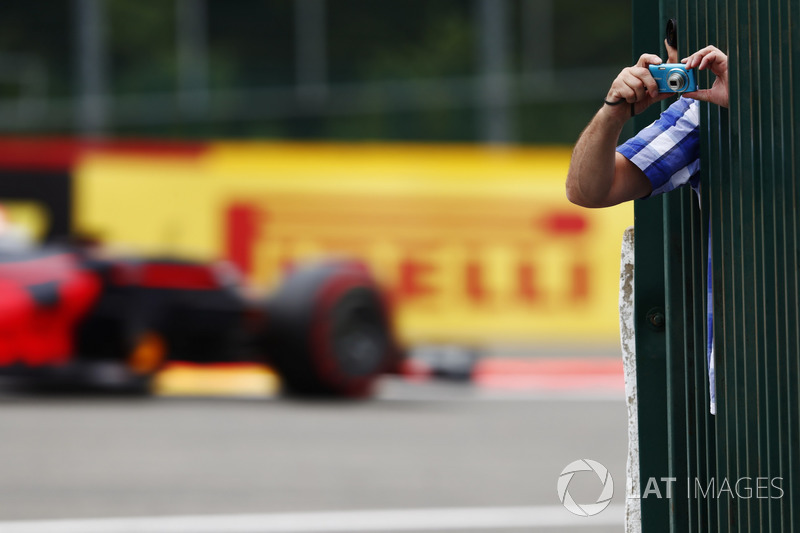 A fan leans out to take some photos as Max Verstappen, Red Bull Racing RB13, passes through the background