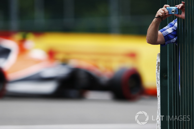 A fan leans out to take some photos as, as Stoffel Vandoorne, McLaren MCL32, passes through the background