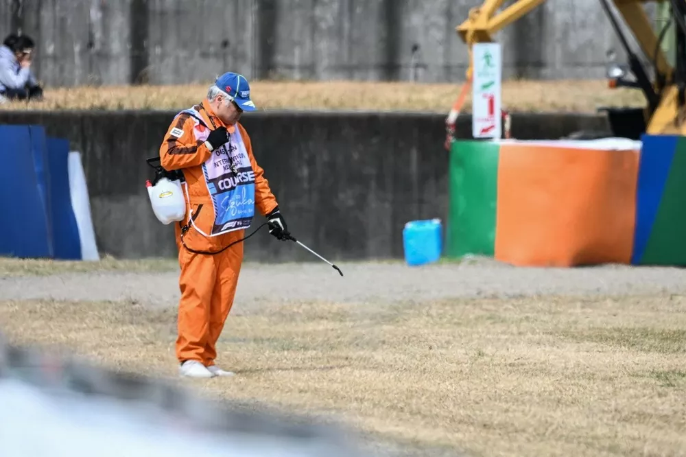 A track marshal waters down the dried out grass along the side of the track