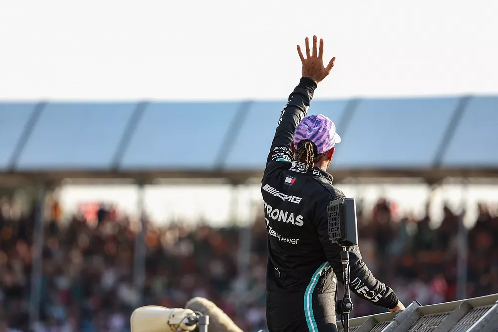 Pole man Lewis Hamilton, Mercedes, climbs a catch fence to wave to fans