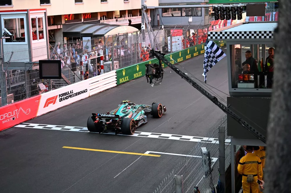 Fernando Alonso, Aston Martin AMR24, passes the chequered flag waved by Kylian Mbappe