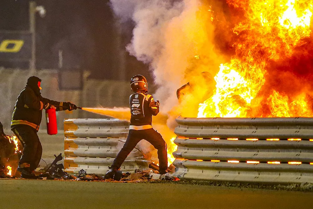 Fire marshals deal with the flames and a medical delegate assists Romain Grosjean, Haas F1, after a huge crash on the opening lap
