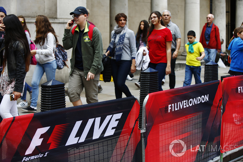 Members of the public walk past railings covered in F1 Live branding