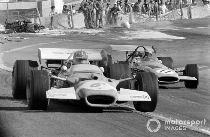 Graham Hill, Lotus 49C Ford, leads Bruce McLaren, McLaren M14A Ford, pasan a los oficiales que trabajan para retirar un coche quemado