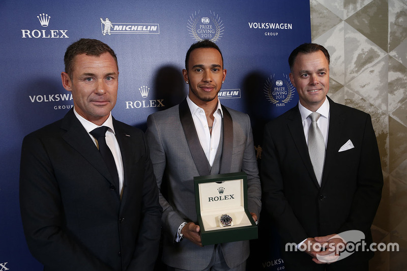 Lewis Hamilton obtiene un reloj Rolex, flanqueado por Tom Kristensen.